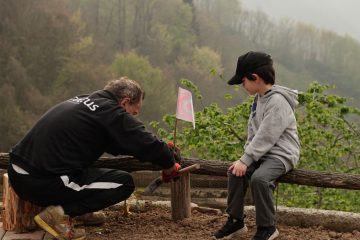 An older man and a boy engage in outdoor activities in a foggy rural setting, surrounded by nature.