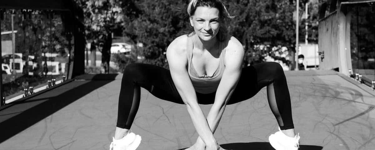 Woman in sports attire doing a crouching stretch on a bridge, black and white photo.
